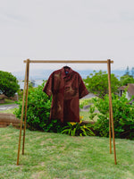 Upena aloha shirt in wine red hanging on a wooden clothing rack